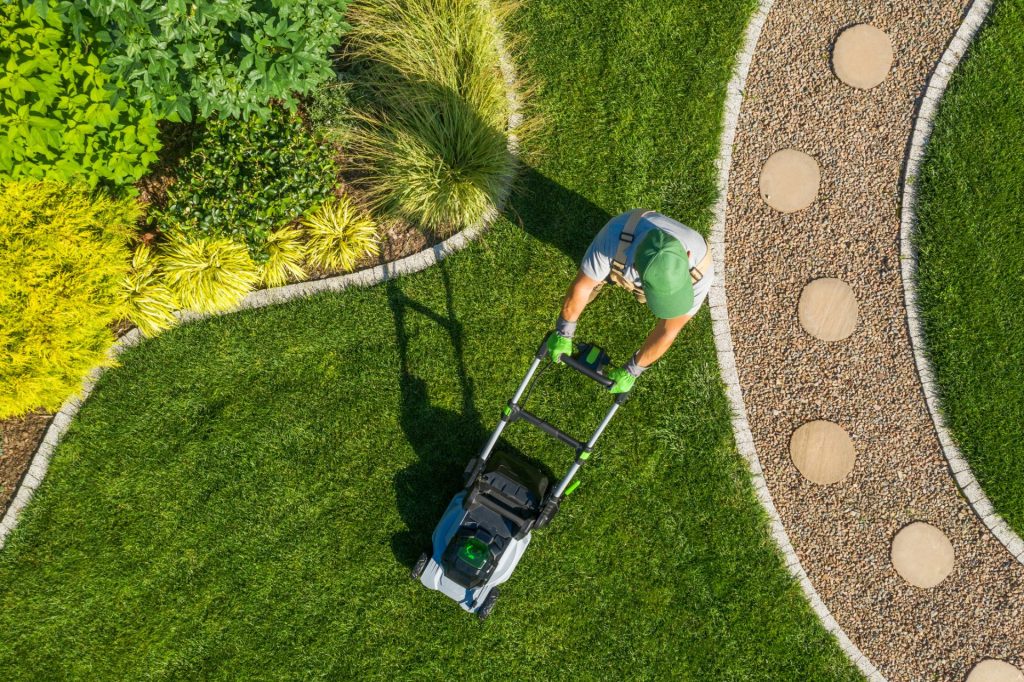 Aerial view of a gardener mowing a backyard lawn