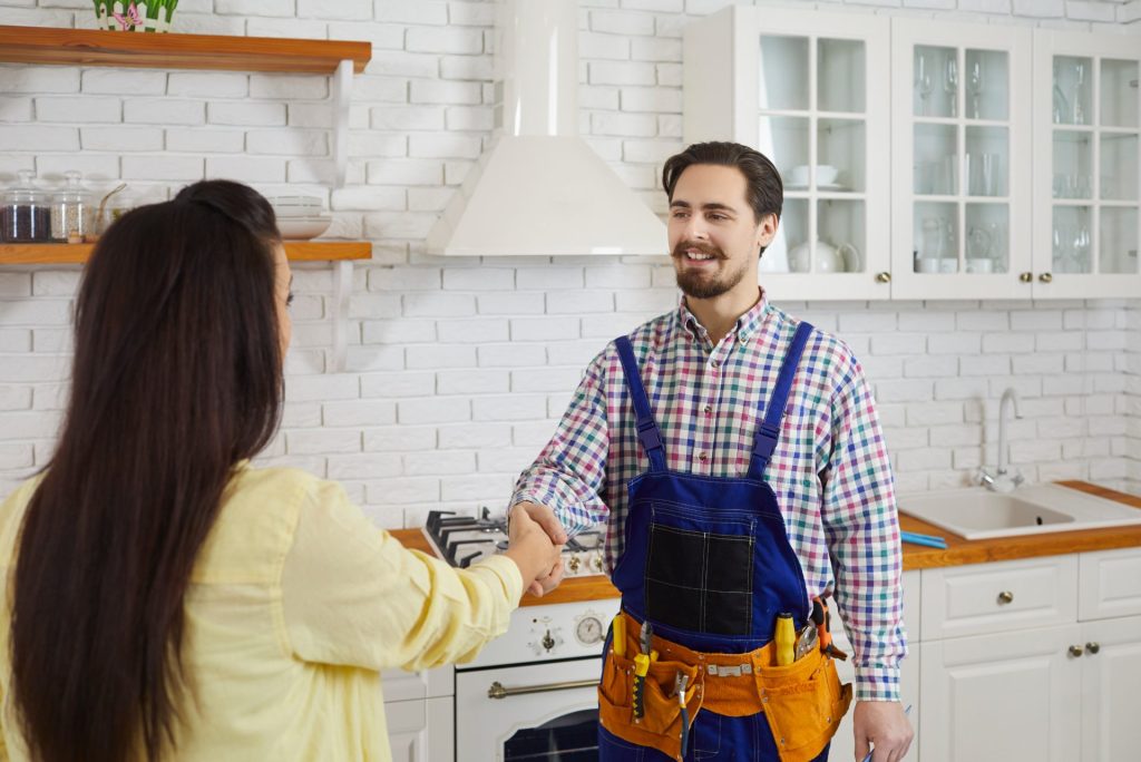 Plumber shaking hands with a happy customer in a kitchen