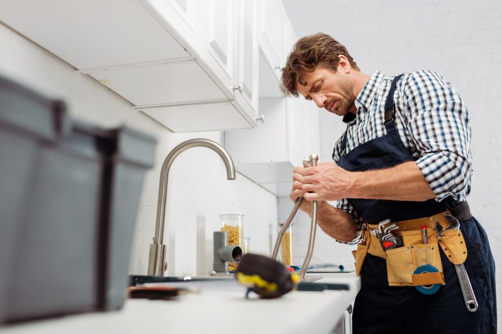 Plumber working on pipes under a kitchen faucet with tools