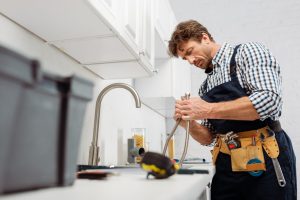 Plumber working on pipes under a kitchen faucet with tools
